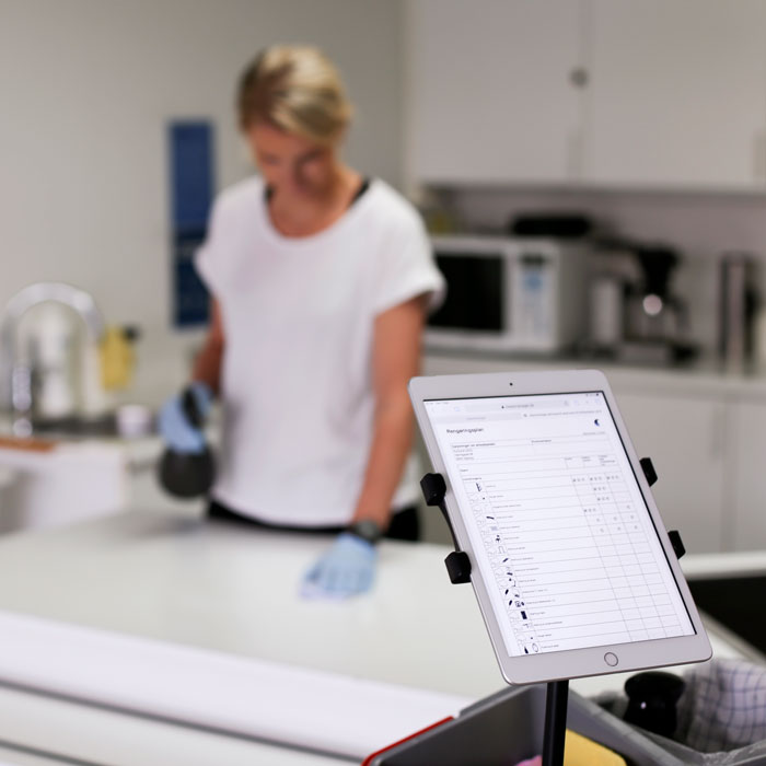 Cleaner using a tablet with a digital cleaning plan, illustrating organised work planning and documentation.